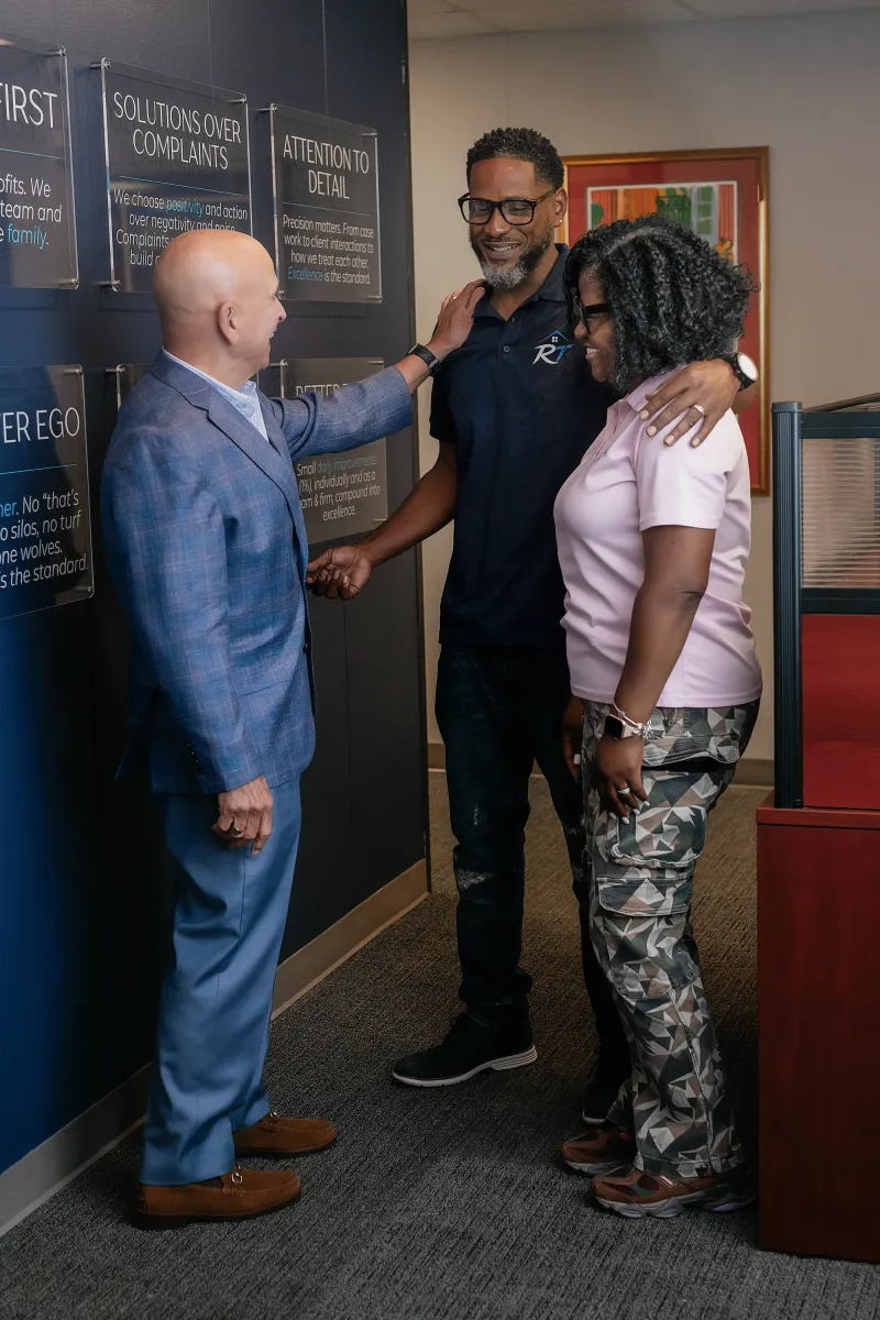 Chip Forstall greeting two clients in front of the firm's values wall