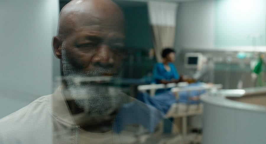 man in window looking at motorcycle accident person on hospital bed.