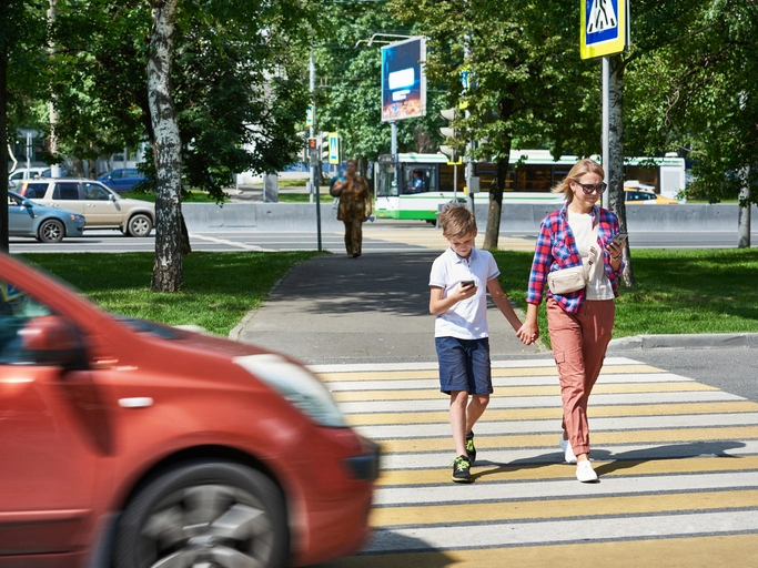 Mother and child crossing a pedestrian crosswalk while distracted by mobile phones as a car approaches nearby