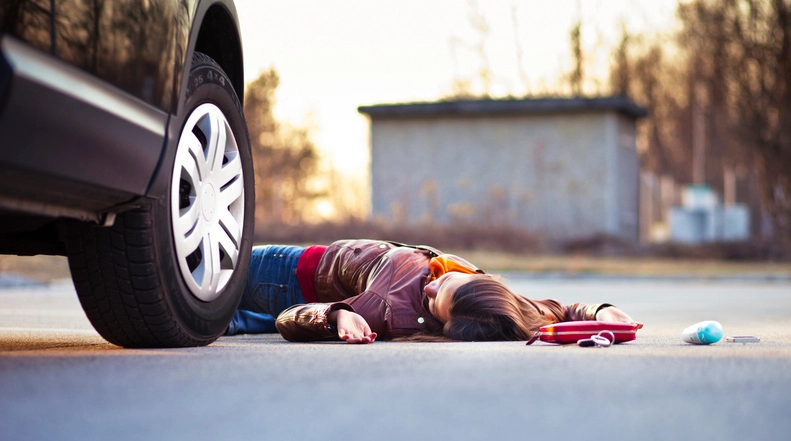Injured pedestrian lying on the roadway beside a vehicle after a serious traffic accident